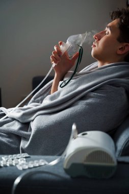 Evde hastalık tedavisi için kompresör nebulizatörü kullanılıyor. Öksürük tedavisi için oksijen maskesi takan bir adam.