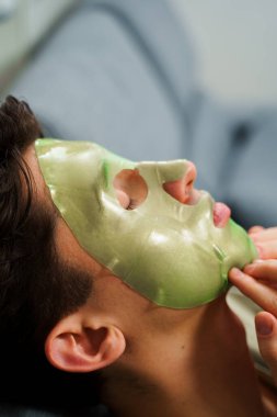 Adam yaşlanmayı önleyen bakım için yüz maskesi takıyor. Evde yeşil maskeli kırışıklık önleme prosedürü