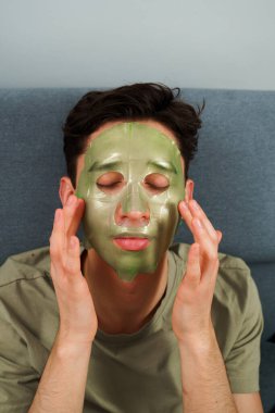 Adam yaşlanmayı önleyen bakım için yüz maskesi takıyor. Evde yeşil maskeli kırışıklık önleme prosedürü