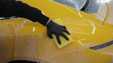 4K otomobil garajında sabun ve süngerle sarı spor arabayı elden incelemek. Oto yıkama, yıkama, sabun ve suyu özel temizlik ve boya hizmetleri için kullanma