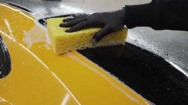 Oto yıkama, yıkama, sabun ve suyla temizleme ve boyama 4K video. Otomobil garajında sabun ve süngerle sarı spor arabayı elden incelemek.