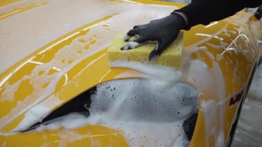 Oto yıkama, yıkama, sabun ve suyla temizleme ve boyama 4K video. Otomobil garajında sabun ve süngerle sarı spor arabayı elden incelemek.