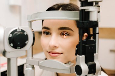 Kesik lambalı bir oftalmolog kadının gözlerini ve korneasını inceliyor. Göz doktoru, göz ve kornea teşhisi koymak için kesik lambadan gelen ışıkla hastanın gözünü aydınlatıyor.