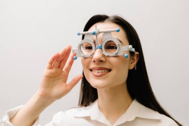 Beyaz arka planda gözlüklü bir kız. Kısa veya uzun görüşlü bir kızın göz görme sistemini incelemek için deneme gözlüğü seçimi için oftalmolog muayenesi