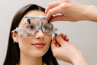 Kız göz muayenesi için göz doktorunun gözlük takıyor. Doğru reçeteli lensleri belirlemek için deneme çerçevesi gözlüğü