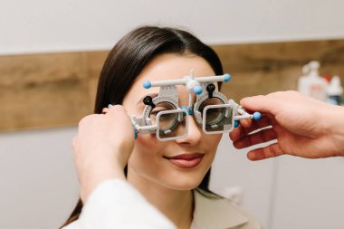 Kız göz muayenesi için göz doktorunun gözlük takıyor. Doğru reçeteli lensleri belirlemek için deneme çerçevesi gözlüğü