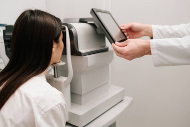 Modern otorefraktör ve OKT makineleriyle göz muayenesi. Otomatik fraktör kırılma hatalarını ölçer, gözlük veya lens reçetelerinin yüksek doğruluk ve verimlilikle belirlenmesine yardımcı olur