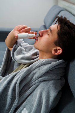Adam üşümüş ve yatakta uzanıp burnunu burun spreyiyle siliyor. Adam burun spreyi kullanıyor ve hastalık tedavisi için ilaç ve ilaç alıyor.