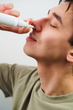 Adam grip için burun spreyi kullanıyor. Hasta beyaz arka planda sinüzit tedavisi için burun damlası alıyor.