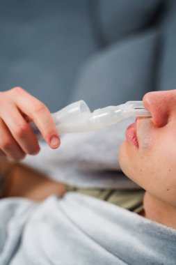 Astım krizi geçiren genç bir adam solunum cihazıyla nefes alıyor. Evde nebulizörle burun solumuş.