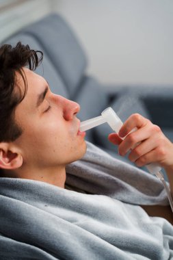 Hasta adam evde grip tedavisi için ağız spreyi nebulizatörü kullanıyor. Evde nebulizatörün yardımıyla ağız solunumu.