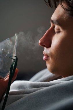 Evde hastalık tedavisi için kompresör nebulizatörü kullanılıyor. Öksürük tedavisi için oksijen maskesi takan bir adam.