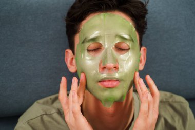 Adam yaşlanmayı önleyen bakım için yüz maskesi takıyor. Evde yeşil maskeli kırışıklık önleme prosedürü