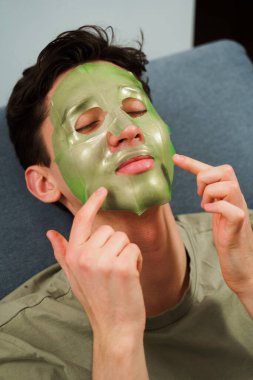 Evde yüzün sulansın diye maske takan rahat bir adam. Adam cilt bakımını yenilemek için maske takıyor.