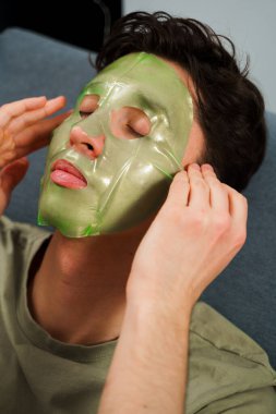 Evde yüzün sulansın diye maske takan rahat bir adam. Adam cilt bakımını yenilemek için maske takıyor.