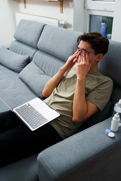 Tired IT specialist with headache in front of laptop. Eye tiredness from working remotely at home