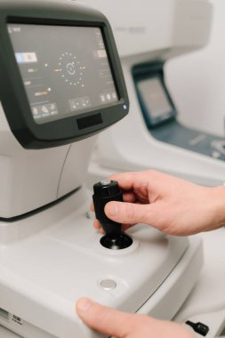 Göz muayenesi sırasında otomatik fraktörü ayarlayan bir optometristin yakın çekimi. Otomatik izleyici, görme düzeltmesi ve göz sağlığı değerlendirmesi için kesin ölçümler sunar