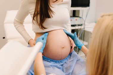 Jinekolog klinikte kontrol sırasında hamile kadının karnını muayene ediyor. Rahmin elle muayene edilmesi, jinekoloji kliniğinde bebek fetüs embriyosu çıkıntıları.