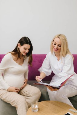 Jinekolog randevusu sırasında hastaya yüksek hemoglobin ve kan basıncı hakkında danışmanlık yapmak. Jinekolog, hamile bir kadının kan testinin sonuçlarını tartışıyor.