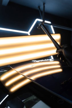 PDR teknisyeni, kaputtaki çukur düzeltmesini kontrol etmek için yansıma lambasına özel bir çekiç tutuyor. Acısız bir araba göçüğü.