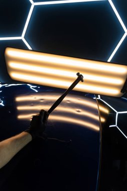 PDR teknisyeni, kaputtaki çukur düzeltmesini kontrol etmek için yansıma lambasına özel bir çekiç tutuyor. Acısız bir araba göçüğü.