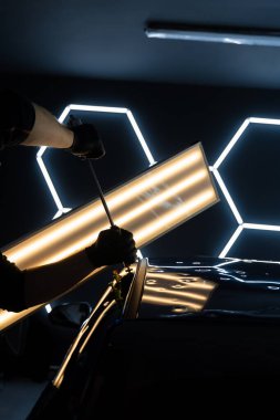 Ağrısız araba göçüğü teknisyeni, araba gövdesi panellerini onarmak için tutkal şeritlerine sürgülü çekiç kullanıyor. PDR Ayrıntılı yansıma çizgileri kusursuz yüzey restorasyonu için hassas çekme kılavuzu