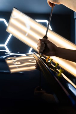 Ağrısız araba göçüğü teknisyeni, araba gövdesi panellerini onarmak için tutkal şeritlerine sürgülü çekiç kullanıyor. PDR Ayrıntılı yansıma çizgileri kusursuz yüzey restorasyonu için hassas çekme kılavuzu