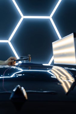 Kontrollü güç, boya hasarı olmadan yüzeyi onarır. PDR sürgülü çekiç, yeniden boyanmamış araba göçüğü. PDR teknisyeni araba panelinden yapışkan şeritler ve çekiç kullanarak bir çukur açtı.