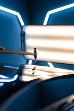 PDR teknisyeni, çarpma aletini ve çekiç kombinasyonunu dolu izlerini düzeltmek için kullanır. Odaklanmış vuruşlar boyaya zarar vermeden metali yeniden hizaladı. Devrilmiş bir aletle kontrol edilen musluklar dolu ile bükülmüş metali yeniden şekillendirir