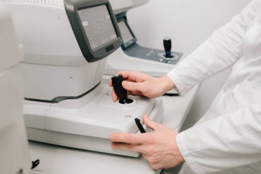 Göz muayenesi sırasında otomatik fraktörü ayarlayan bir optometristin yakın çekimi. Otomatik izleyici, görme düzeltmesi ve göz sağlığı değerlendirmesi için kesin ölçümler sunar