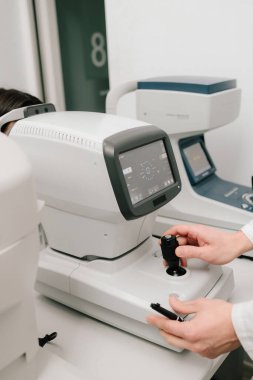 Otomatik fraktör görme düzeltmesi ve göz sağlığı değerlendirmesi için kesin ölçümler sağlar. Göz muayenesi sırasında otomatik fraktörü ayarlayan bir optometristin yakın çekimi.