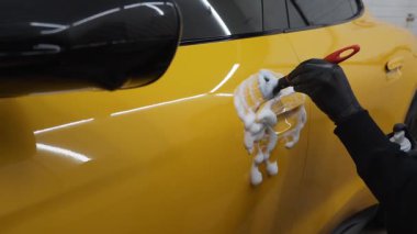 4K video 'da araba yıkama seansında deterjan uygulaması. İşçi araba kapısını köpük ve deterjanla fırçayla temizliyor