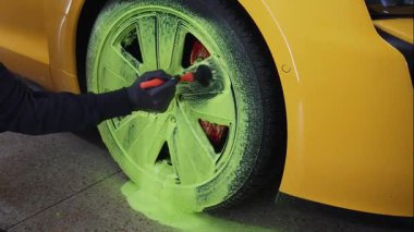 Temizlikçi araba lastiklerini yeşil köpükle yıkıyor. 4K video 'da deterjanla fırça kullanıyor. Araç bakımı için serviste ayrıntılı prosedür