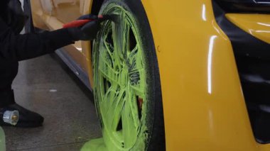 4K video servisindeki araba bakımı prosedürü. Temizlikçi araba lastiklerini yeşil köpükle yıkıyor. Oto yıkamada deterjanla fırça kullanıyor.