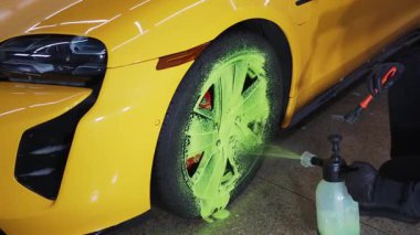 4K video servisindeki araba bakımı prosedürü. Temizlikçi araba lastiklerini yeşil köpükle yıkıyor. Oto yıkamada deterjanla fırça kullanıyor.