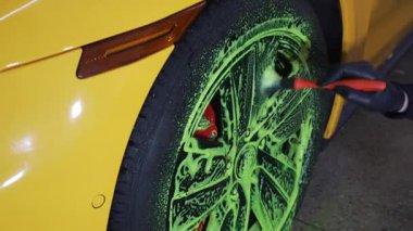 Temizlikçi araba lastiklerini yeşil köpükle yıkıyor. 4K video 'da deterjanla fırça kullanıyor. Araç bakımı için serviste ayrıntılı prosedür