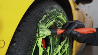 4K video servisindeki araba bakımı prosedürü. Temizlikçi araba lastiklerini yeşil köpükle yıkıyor. Oto yıkamada deterjanla fırça kullanıyor.