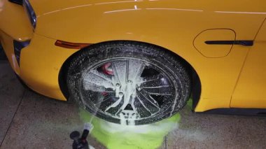 Araba yıkama videosundaki yeşil sabunla tekerlek temizleme işlemi. Adam servisteki araba tamiri için yeşil sabun solüsyonu kullanıyor.