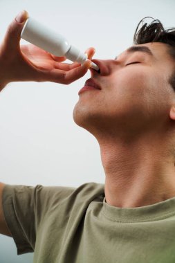 Adam grip için burun spreyi kullanıyor. Hasta beyaz arka planda sinüzit tedavisi için burun damlası alıyor.