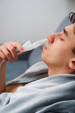 Astım krizi geçiren genç bir adam solunum cihazıyla nefes alıyor. Evde nebulizörle burun solumuş.