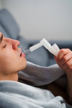Hasta adam evde grip tedavisi için ağız spreyi nebulizatörü kullanıyor. Evde nebulizatörün yardımıyla ağız solunumu.