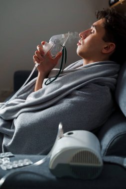 Evde hastalık tedavisi için kompresör nebulizatörü kullanılıyor. Öksürük tedavisi için oksijen maskesi takan bir adam.