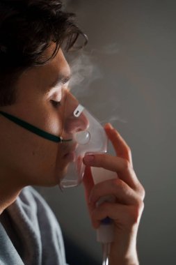 Evde hastalık tedavisi için kompresör nebulizatörü kullanılıyor. Öksürük tedavisi için oksijen maskesi takan bir adam.