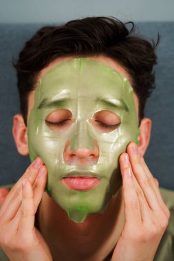Adam yaşlanmayı önleyen bakım için yüz maskesi takıyor. Evde yeşil maskeli kırışıklık önleme prosedürü