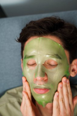 Adam yaşlanmayı önleyen bakım için yüz maskesi takıyor. Evde yeşil maskeli kırışıklık önleme prosedürü