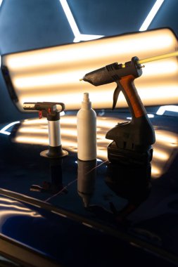 Yapıştırıcı tabancası, PDR sprey şişesi ve PDR tamiri için ısıtma aletleri. Yüksek güçlü tutkal tabancası, ısı kaynağı ve PDR temizlik aletleri stüdyo ışıkları altında hassas oto tamirine hazırdır.