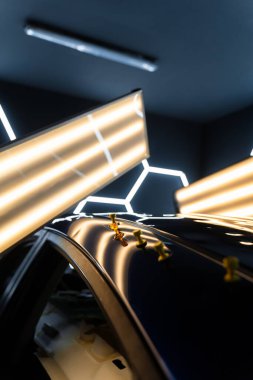 Ağrısız çukur onarma işlemi sırasında LED ışıklarının altındaki çökmüş bir arabanın çatısına birden fazla yapıştırıcı şeridi takılmış. Yapıştırıcı sekmeleri yüzeyi hatasız bir bitiş için hizalamaya ve onarmaya yardımcı olur