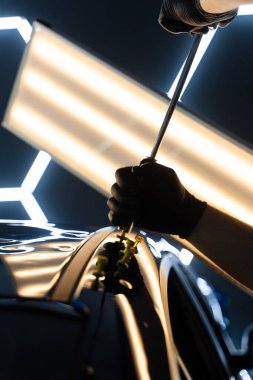 PDR Ayrıntılı yansıma çizgileri kusursuz yüzey restorasyonu için hassas çekme kılavuzu. Ağrısız araba göçüğü teknisyeni, araba gövdesi panellerini onarmak için tutkal şeritlerine sürgülü çekiç kullanıyor.