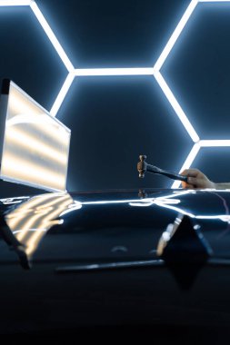 PDR teknisyeni, yapıştırıcı şeritleri ve çekiçle arabanın panelini göçertti. Kontrollü güç, boya hasarı olmadan yüzeyi onarır. Bir PDR sürgülü çekiç yeniden boyanmadan araba göçüğü