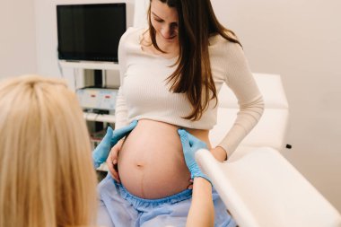 Rahmin elle muayene edilmesi, jinekoloji kliniğinde bebek fetüs embriyosu çıkıntıları. Jinekolog klinikte kontrol sırasında hamile kadının karnını muayene ediyor.